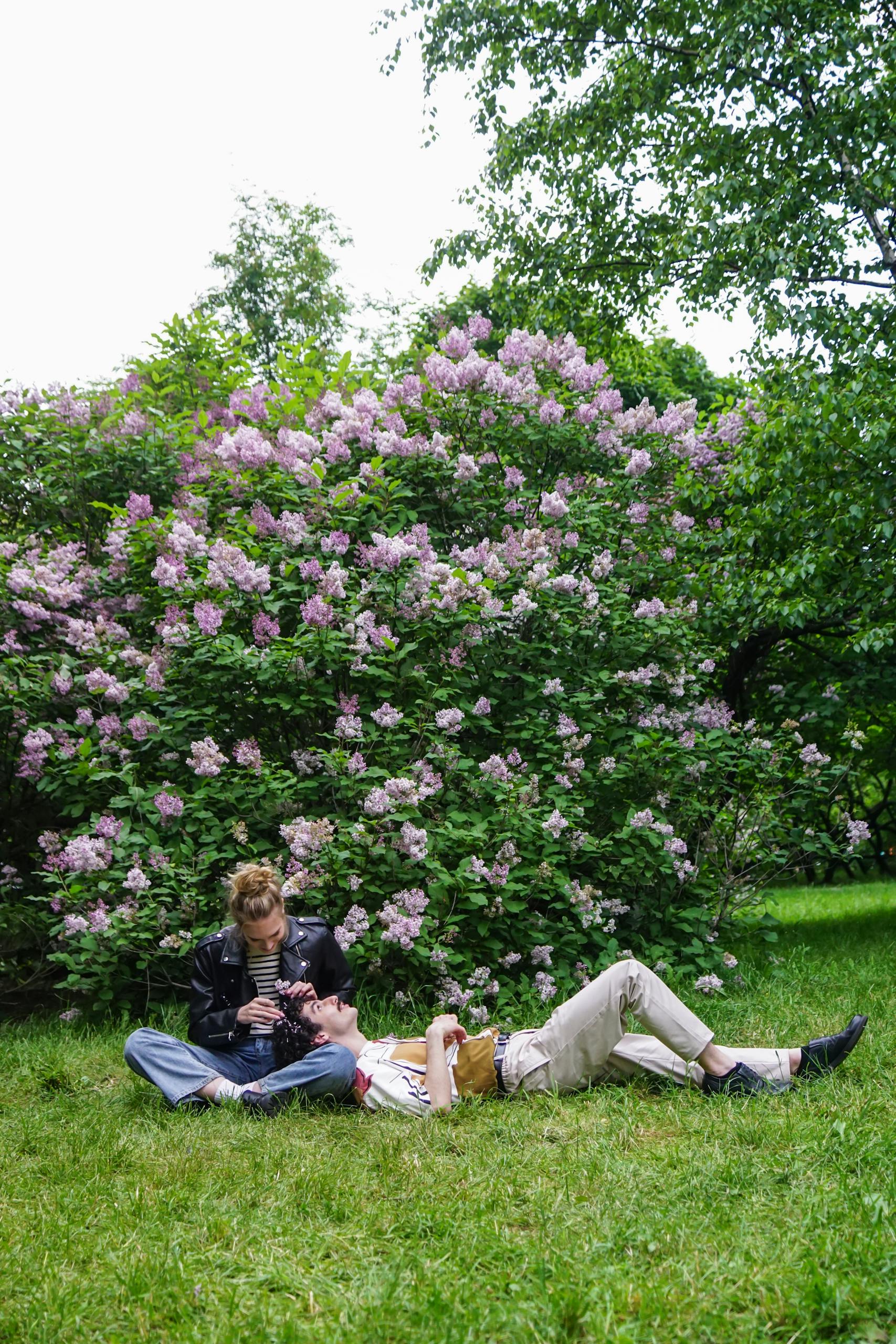 Breathwork A couple enjoying a peaceful moment in a park, sitting near a blooming lilac bush.