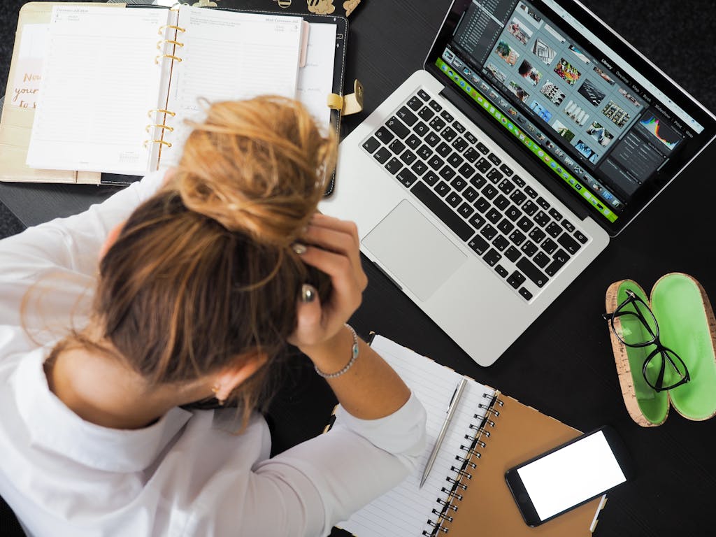 Breathwork Overhead view of a stressed woman working at a desk with a laptop, phone, and notebooks.
